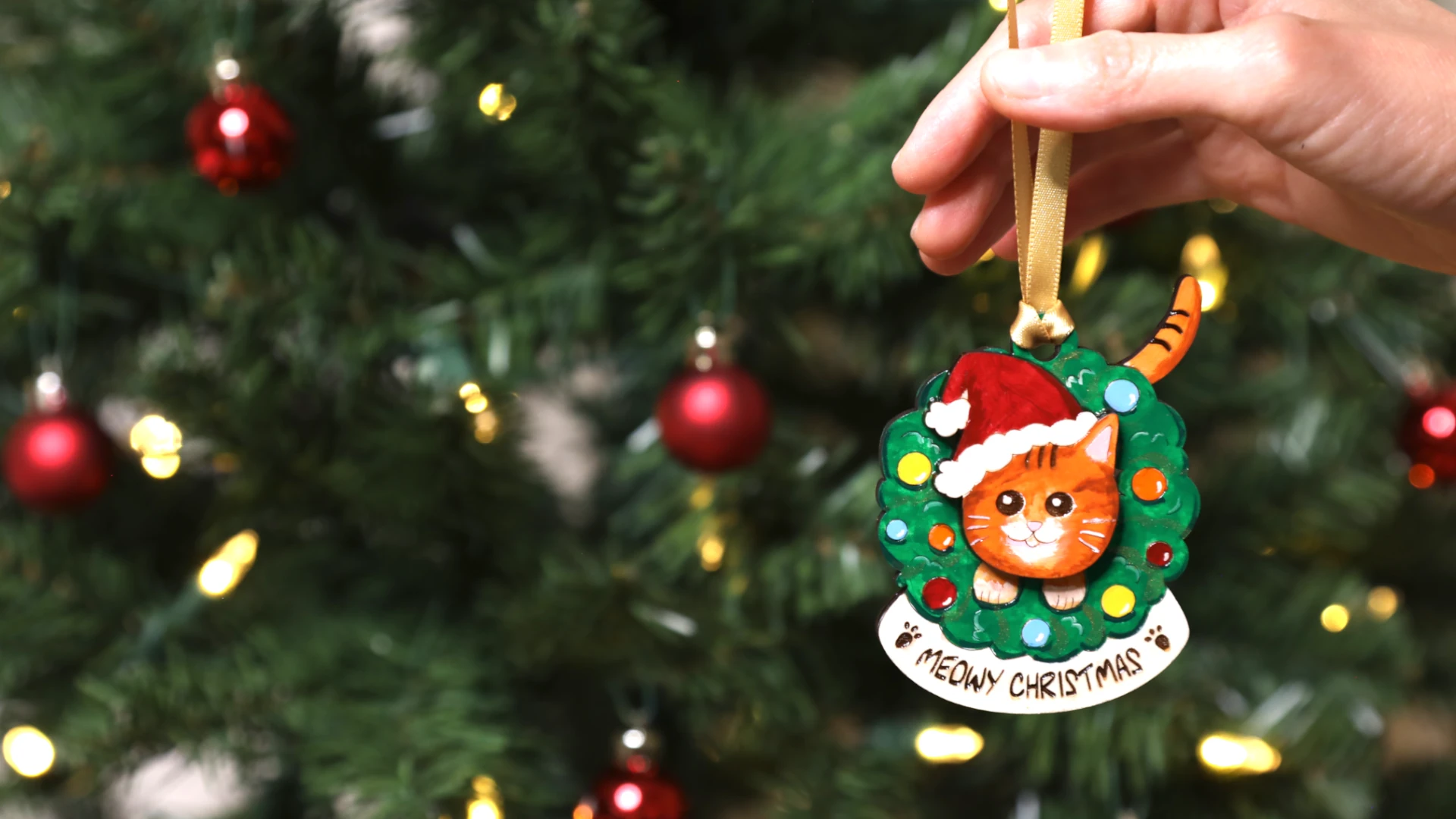 hand painted cat ornament held in front of a Christmas tree